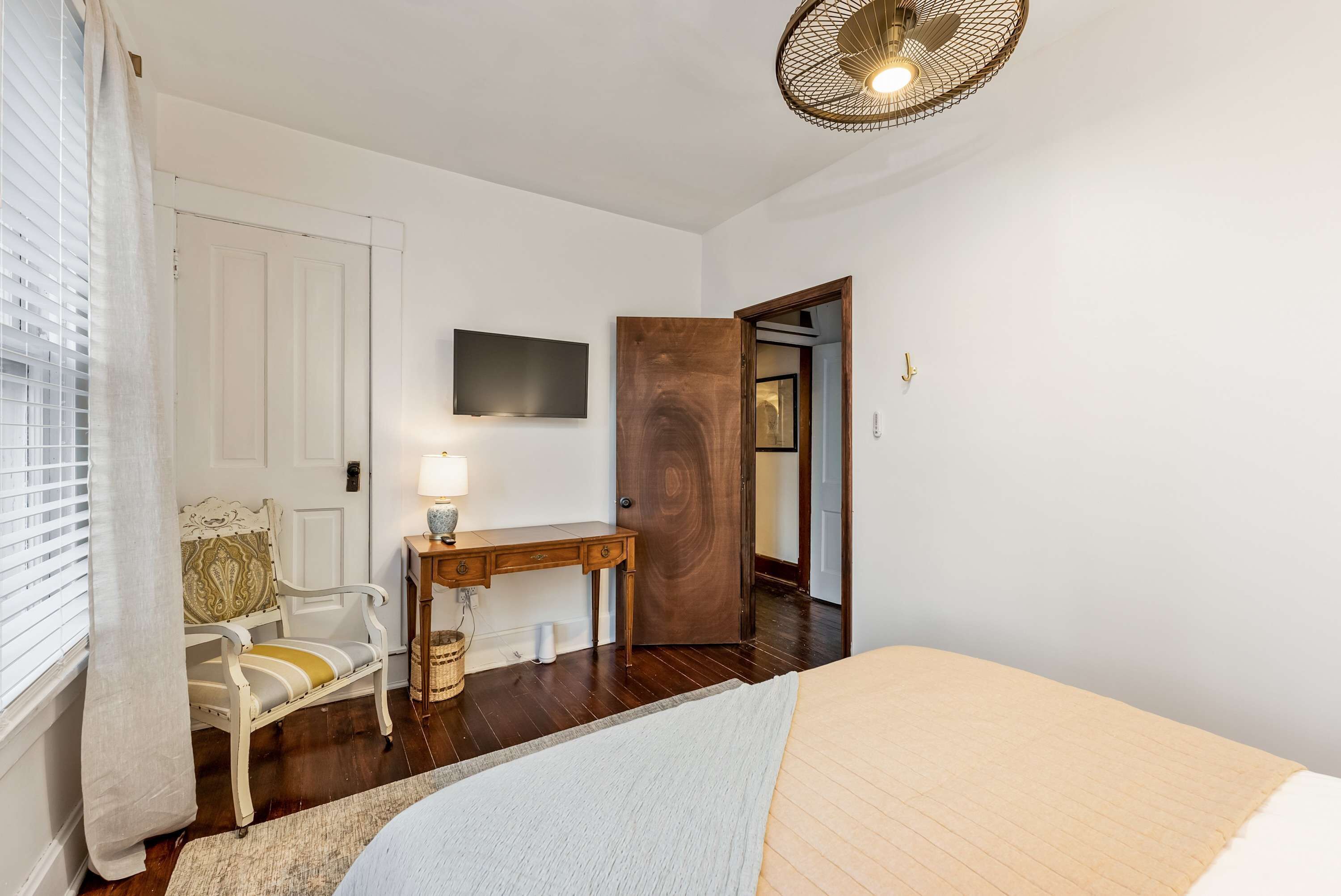 A bedroom with a bed, a desk with a lamp, a chair, and a television on the wall.