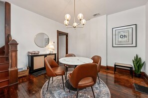 A dining area with a round table, brown leather chairs, a chandelier, a mirror, a framed sign, a potted plant, and a staircase. - German Charm 1 Beautiful Home! (Columbus)