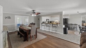 A spacious living area with a dining table, bar stools, and a kitchen area with white cabinets and appliances. - BIG WATER views in Abbeville: 3BR, Master Ste, Hot Tub, Ice Machine, Beach Area (Abbeville)