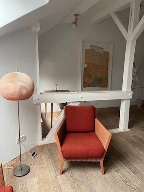 A room with a red chair, a floor lamp, and a painting on the wall.