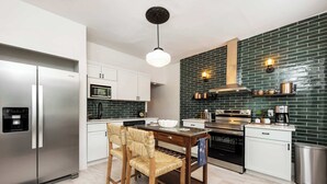A modern kitchen with a stainless steel refrigerator, a microwave, a stove, and a dining area with a wooden table and chairs. - German Charm 2 Sophistication! (Columbus)