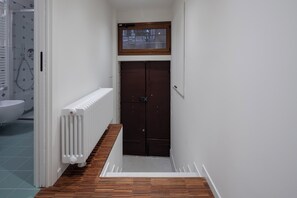 A narrow hallway with a white radiator, a wooden floor, and a brown door with a window above it.