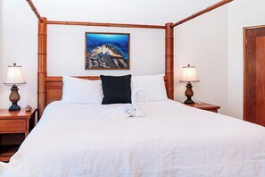 Un lit à baldaquin avec une couvre-lit blanche, deux oreillers noirs et une serviette blanche disposée sur le lit. Un tableau représentant une tortue de mer est accroché au mur, au-dessus du lit.