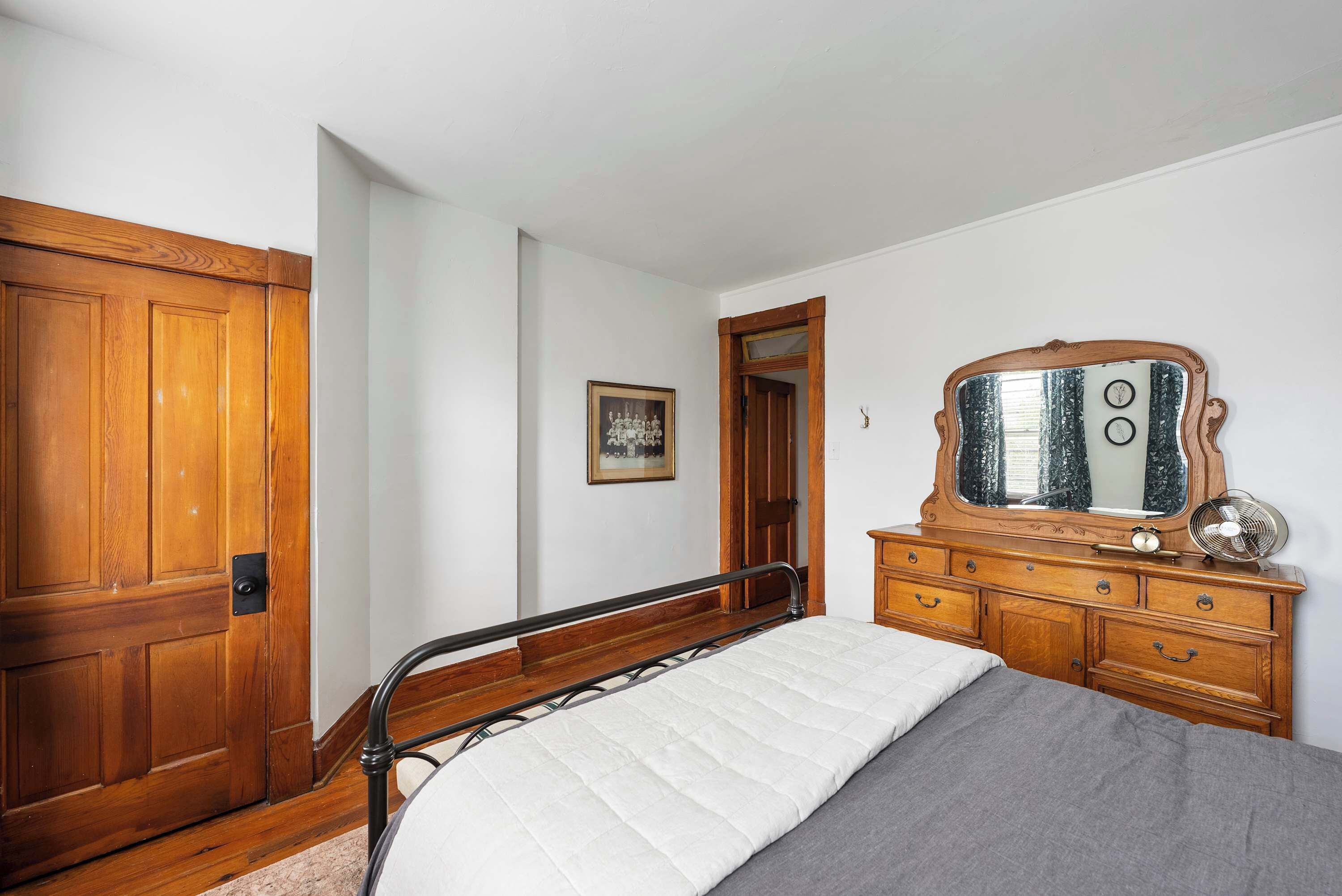 Une chambre avec une porte en bois, une commode avec un miroir et un lit avec un matelas blanc.