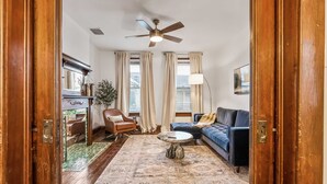 A living room with a wooden floor, a ceiling fan, a sofa, a coffee table, a chair, and a lamp. - German Charm Suites Sleeps 8! (Columbus)