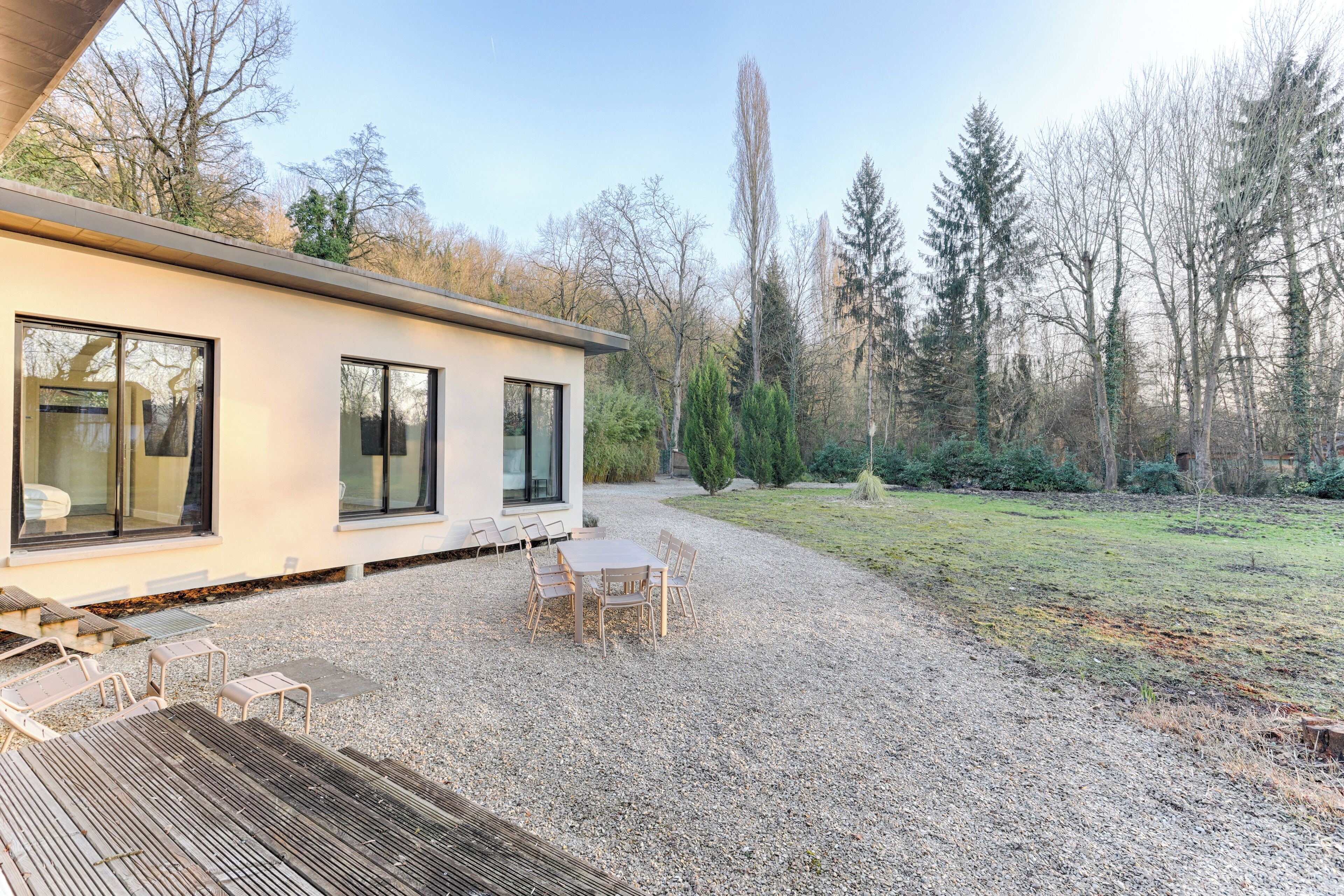 Una casa moderna con un patio, que incluye una mesa y sillas, rodeada por un camino de grava y un césped.