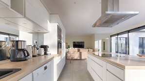 A modern kitchen with a dishwasher, coffee maker, and oven. There is a sofa and a TV in the adjacent living area. - Villa Carotte à 10 Minutes de Disneyland Paris (Chalifert)