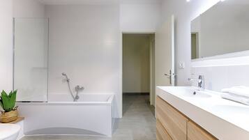 A modern bathroom with a bathtub, a large mirror, and a vanity with a sink.