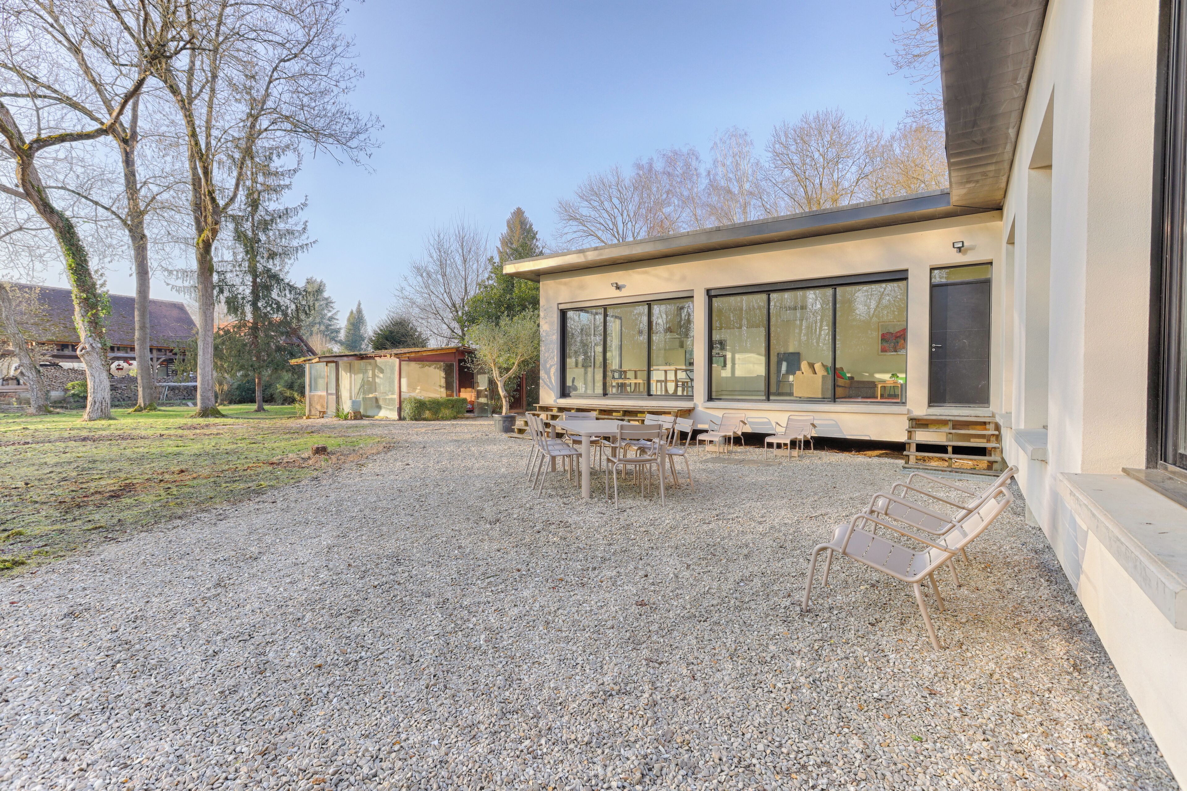 Un bâtiment doté d’une terrasse en gravier, de sièges extérieurs et de grandes fenêtres.