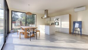 A modern kitchen with white cabinets, a dining area with a wooden table and chairs, and a large window providing natural light. - Villa Carotte à 10 Minutes de Disneyland Paris (Chalifert)