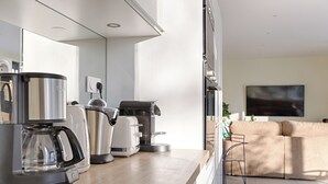 A modern kitchen with a coffee maker, toaster, and kettle. There is a wooden countertop and a view of a living area with a sofa and a TV. - Villa Carotte à 10 Minutes de Disneyland Paris (Chalifert)