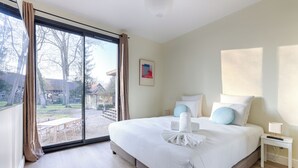 A hotel room with a large bed, a nightstand, a window with curtains, and a view of the outdoors. - Villa Carotte à 10 Minutes de Disneyland Paris (Chalifert)