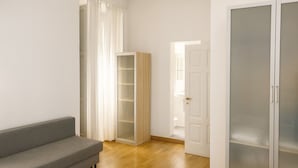 Een moderne woonkamer met een grijze bank, een hoge kast en een schuifdeur naar een badkamer.