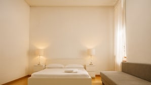 Een minimalistische slaapkamer met een bed, nachtkastjes en een bank.