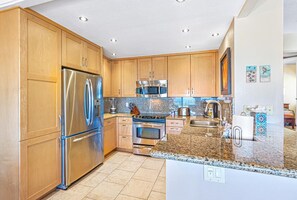 Una cocina moderna con armarios de madera, electrodomésticos de acero inoxidable, encimeras de granito y suelo de baldosas.