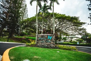 Et stenskilte med en sommerfugllogo og teksten "Kapalua Golf Villas" foran en bygning med græsplæne og palmer.