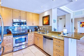 A modern kitchen with granite countertops, stainless steel appliances, wooden cabinets, and a large island with a sink.