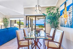 A modern dining area with a glass table and chairs, a blue sofa, and a large plant.