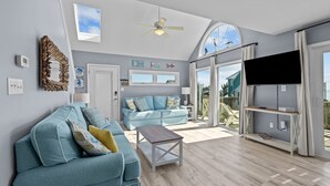 A spacious living room with a light blue sofa, a wooden coffee table, and a ceiling fan. - Bright, spacious oceanfront duplex with pool access (Emerald Isle)
