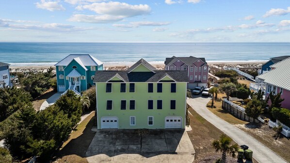 A beachfront property with a large house featuring a garage, a covered porch, and a view of the ocean. - Bright, spacious oceanfront duplex with pool access (Emerald Isle)