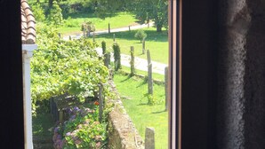A window view of a garden with a stone wall, a wooden fence, and a pathway. - O lagar de Jesús (Padron)