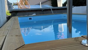 Ein Schwimmbecken mit Holzterrasse, einem Metallarmaturen und blauem Himmel im Hintergrund.