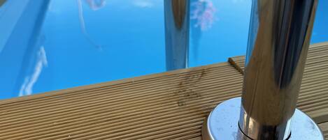 Une terrasse en bois avec un bord de piscine en métal.