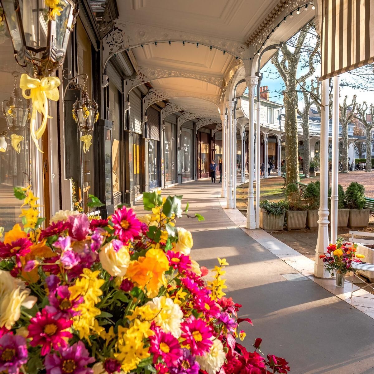 Une allée couverte, agrémentée de colonnes blanches décorées et de compositions florales.