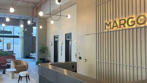A reception area with a modern design, featuring a reception desk, a seating area with a sofa and chairs, and a wall-mounted sign that reads "MARGO". - Great New Modern Department Expo GDL (Guadalajara)