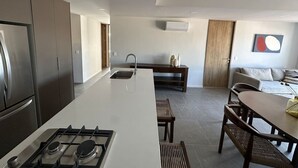 A modern kitchen with a central island, a dining area with a wooden table and chairs, and a seating area with a sofa and cushions. - Luxurious and Spacious Apartment in Centro Zapopan (Zapopan)