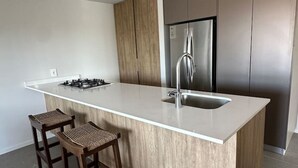 A modern kitchen with a central island, stainless steel appliances, and two wooden bar stools. - Luxurious and Spacious Apartment in Centro Zapopan (Zapopan)