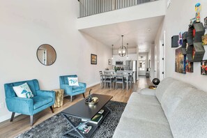 A modern living room with a sofa, two armchairs, a coffee table, and a dining area with a kitchen in the background.