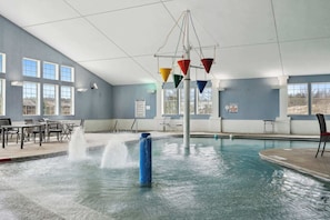 A swimming pool with a water fountain, seating area, and large windows.