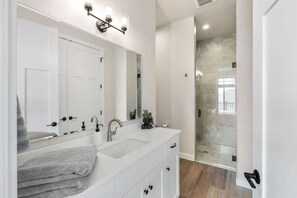 A modern bathroom with a white vanity, a large mirror, a shower with glass doors, and a visible outdoor view.