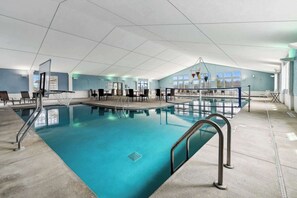 An indoor swimming pool with a clear view of the pool area, a seating area with tables and chairs, and a large window providing natural light.