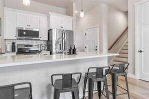 Una cocina moderna con armarios blancos, electrodomésticos de acero inoxidable y una barra con taburetes.