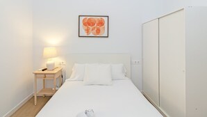 A minimalist hotel room with a bed, a bedside table with a lamp, a wall-mounted artwork, and a wardrobe. - GuestReady - Cozy flat in Valencia (Valencia)