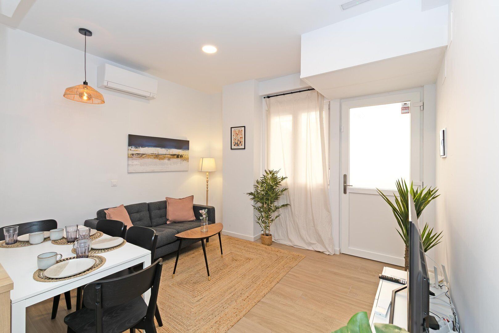 A modern living room with a dining area, featuring a sofa, coffee table, and a large window with curtains.