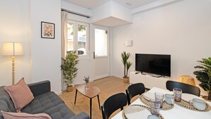 A modern living room with a sofa, a dining table with chairs, a flat-screen TV, and potted plants. - GuestReady - Cozy flat in Valencia (Valencia)