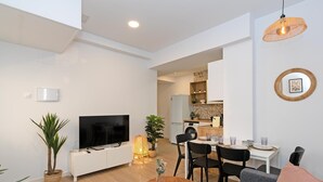 A modern living room with a flat-screen TV, a dining area with a table and chairs, a kitchen with a washing machine, and a small dining table with a few items. - GuestReady - Cozy flat in Valencia (Valencia)