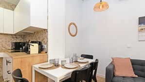A compact living space with a dining table set for four, a kitchenette, a grey sofa, and a hanging light fixture. - GuestReady - Cozy flat in Valencia (Valencia)