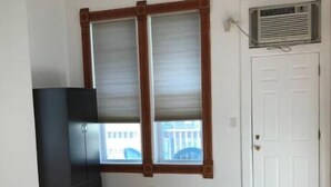 A room with hardwood flooring, a large window with blinds, a white door, and a black entertainment unit. - Spacious loft in the heart of West Town, Noble Square Chicago (Chicago)