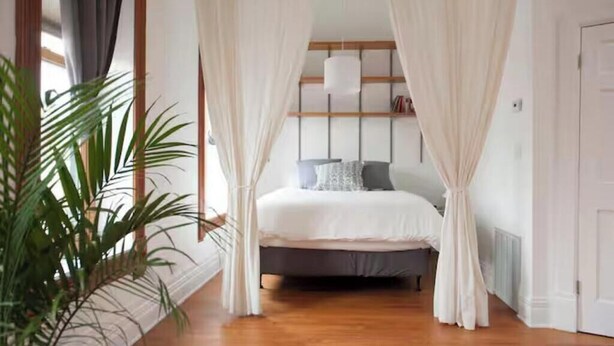 A bedroom with a bed, white curtains, a hanging light, and a potted plant. - Spacious loft in the heart of West Town, Noble Square Chicago (Chicago)