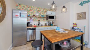 Una cocina compacta con electrodomésticos de acero inoxidable, una mesa de madera y un salpicadero con motivos de frutas.