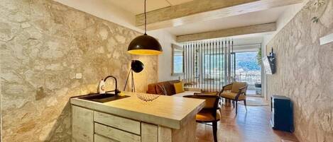 Una cocina moderna con una isla central, paredes de piedra y un amplio ventanal con vistas al exterior.