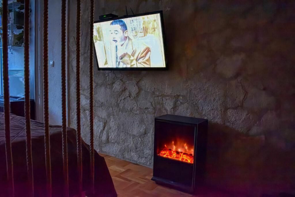 A room with a stone wall, a television mounted on it, and a wood-burning stove.