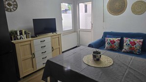 A compact living space with a TV on a wooden cabinet, a sofa with floral cushions, and a dining table with a placemat. - Central, cozy apartment, 50 mts away from the old town in Höxter. (Höxter)