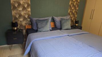 A neatly made bed with a blue quilt, two bedside tables with lamps, and a geometric-patterned wall.