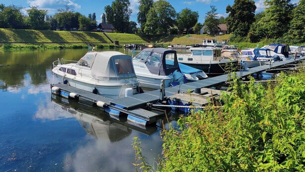 A calm river with boats docked at a pier, surrounded by greenery and trees. - Central, cozy apartment, 50 mts away from the old town in Höxter. (Höxter)