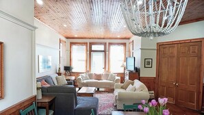 A spacious living room with wooden flooring, a chandelier, and a large wooden door. - Heritage style cottage with lake view, perfect porch for family gatherings. (Port Stanley)
